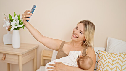 Poster - Mother and daughter sitting on bed breastfeeding baby make selfie by smartphone at bedroom