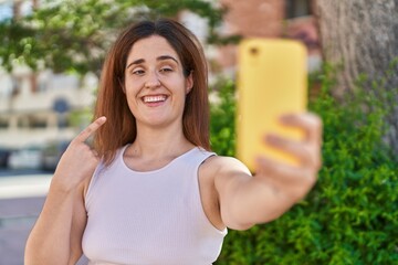 Sticker - Brunette woman taking a selfie photo with smartphone smiling happy pointing with hand and finger