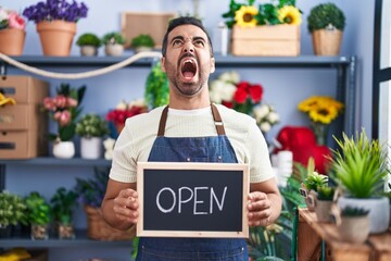 Sticker - Hispanic man with beard working at florist holding open sign angry and mad screaming frustrated and furious, shouting with anger looking up.