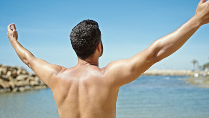 Sticker - Young hispanic man tourist standing shirtless stretching arms at the beach