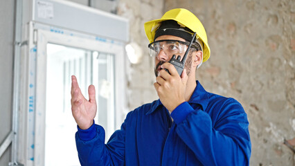 Wall Mural - Young hispanic man worker talking on walkie-talkie at construction site