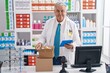 Middle age grey-haired man pharmacist using touchpad holding pills bottle at pharmacy