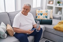 Middle Age Grey-haired Man Using Smartphone Holding Bottle Of Water At Home