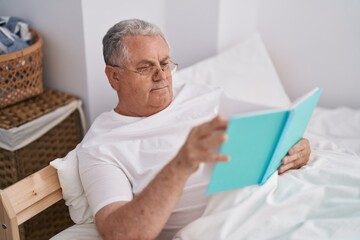 Poster - Middle age grey-haired man reading book sitting on bed at bedroom