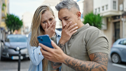 Wall Mural - Man and woman couple using smartphone looking upset at street