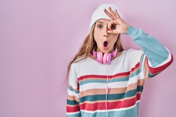 Wall Mural - Young blonde woman standing over pink background doing ok gesture shocked with surprised face, eye looking through fingers. unbelieving expression.