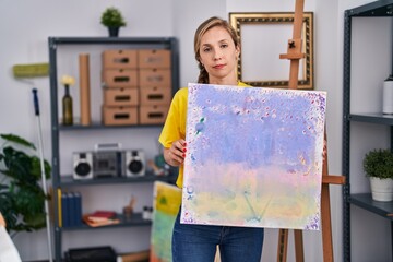 Poster - Young blonde woman holding canvas relaxed with serious expression on face. simple and natural looking at the camera.