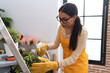 Young arab woman florist using diffuser watering plant at flower shop
