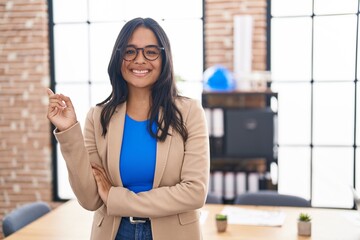 Poster - Brunette woman working at the office wearing glasses smiling happy pointing with hand and finger to the side