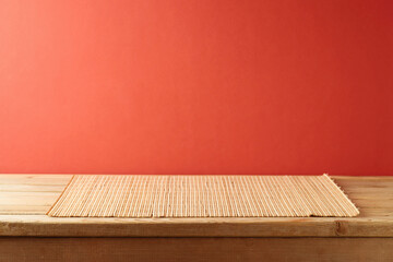 Wall Mural - Empty wooden table with bamboo place mat  over red background. Chinese New Year mock up for design and product display.