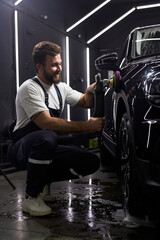 Wall Mural - Auto Mechanic Use polishing tool for Buffing and polishing black car In auto repair shop, side view. Confident male worker in uniform at work place concentrated