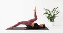 A Woman Performs Leg Rolls With A Yoga Brick, The Exercise Is Aimed At Mastering The Longitudinal Splits, She Trains Alone In Sportswear In A Room Lying On A Mat
