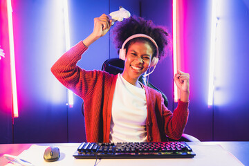 Wall Mural - African American girl gaming streamer team winner playing online fighting with Esport wearing headphones in neon lighting room. Talking other players planing strategies to win competitors. Tastemaker.