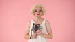 © kinomaster - Portrait of woman with retro video camera in hands close up. Woman looking like in studio on pink background.
