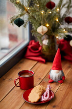 Holidays, Decoration And Celebration Concept - Close Up Of Christmas Gnome, Cup Of Coffee In Red Mug, Ginger Cookies And Candy Canes On Window Sill At Home