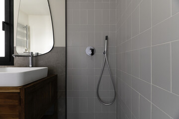 Sticker - Small modern bathroom with gray stone effect tiles, mirror on the wall, white porcelain sink cantilevered over wooden cabinet, shower cubicle with glass screen and chrome taps