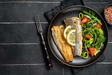 Wall Mural - Roasted sea bass fillet with salad, Branzino fish. Black background. Top view. Copy space