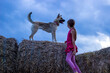 Cute little girl in pink dress is standing on top of hay bale with her dog