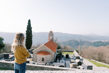 Young Woman Looks At The Church Of St. Nicholas And The Cemetery Around It. Baosici, Montenegro. Back View
