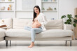 © New Africa - Beautiful pregnant woman sitting on sofa at home