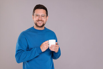 Poster - Portrait of happy man holding white mug on grey background. Space for text