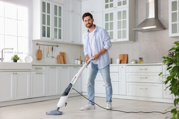 Poster - Happy man cleaning floor with steam mop in kitchen at home