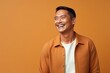 © igolaizola - happy asian man laughing and looking up at copy space on orange background