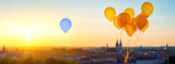 Standing out from the crowd concept. Blue balloon floating over a city separately from golden tied balloons during sunset
