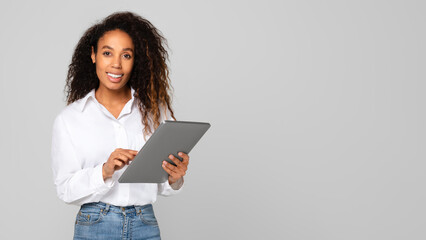 Black millennial lady using her digital tablet gadget, gray background