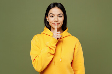 Wall Mural - Young secret happy cool Latin woman wears yellow hoody casual clothes say hush be quiet with finger on lips shhh gesture isolated on plain pastel green background studio portrait. Lifestyle concept.