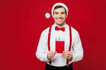 Poster - Merry traveler man wears white shirt Santa hat hold passport ticket isolated on plain red background Tourist travel abroad in free time rest getaway. Air flight trip, Happy New Year Christmas concept.