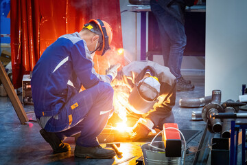 Poster - Welders at work. Men use soldering machine. Welders in production room. Guy covers eyes with hand so as not to look at welding. Welders do metal processing. Men in production workshop