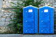 Public portable bio WC cabins by stone wall on city street. Mobile toilets installed for guests in urban park. Blue sanitary units in town