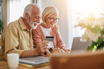 Senior couple sit at a table in the living room with laptop,working from home office