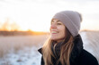 Backlit Portrait of calm happy smiling free woman with closed eyes enjoys a beautiful moment life on the fields in winter time with snow at sunset or dawn