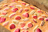 Fototapeta Na ścianę - A freshly baked strawberry and rhubarb cake, sprinkled with sugar dusting, captures the essence of summer with its vibrant colors and rich texture.