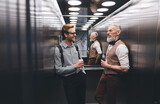 Fototapeta  - Positive businessman talking with elderly colleague by modern elevator