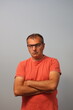 © Ivelin - A self-assured middle-aged man, sporting eyeglasses and crossing his arms, is dressed in an orange t-shirt against a plain gray background.