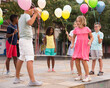 Multiracial group of cheerful preteen children having fun together outdoors on summer day, playing chinese jump rope with colorful toy balloons in hands