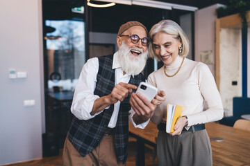 Cheerful elderly colleagues browsing smartphone together in office