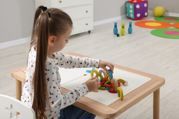 Wall Mural - Motor skills development. Girl playing with colorful wooden arcs at white table in kindergarten