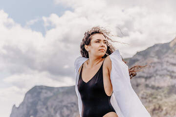 Woman on a yacht. Happy model in a swimsuit posing on a yacht against a blue sky with clouds and mountains