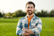 Portrait of smiling bearded man farmer with crossed arms standing in field, outdoors