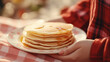 Women holding white plate with pile pancakes