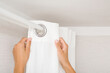 Young adult woman hands hanging clean white thick night curtains in rings on rod at home room. Closeup. Point of view shot.