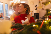 Boy Kissing And Hugging Mother Near Christmas Tree At Home