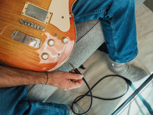Man Plugging Cable In Guitar At Home