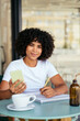 © Westend61 - Smiling woman holding smart phone and pen at sidewalk cafe