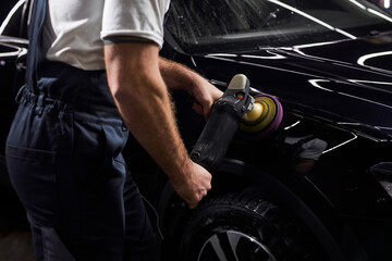 male auto repair man doing car polish with machine, professional auto detailer hand holding rotary polisher while polishing paint surface of shiny black car. Car detailing, car wash