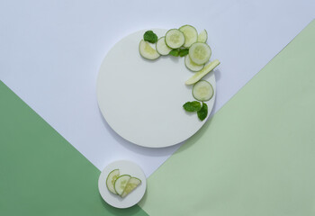 Wall Mural - Fresh cucumber slices and mint leaves displayed on white round podium on paper background. Creative background for advertising cosmetics product with ingredient from natural